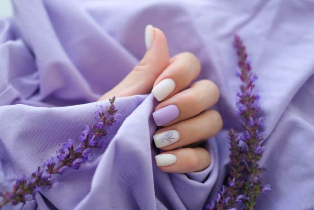 A woman's hand with white square nails and lavender accent nail 