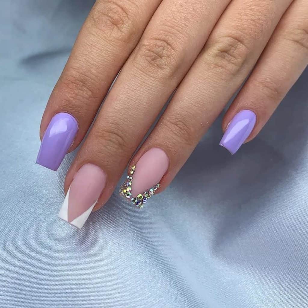 A woman's hand having a lavender colored nail polish with crystals and angled lines 