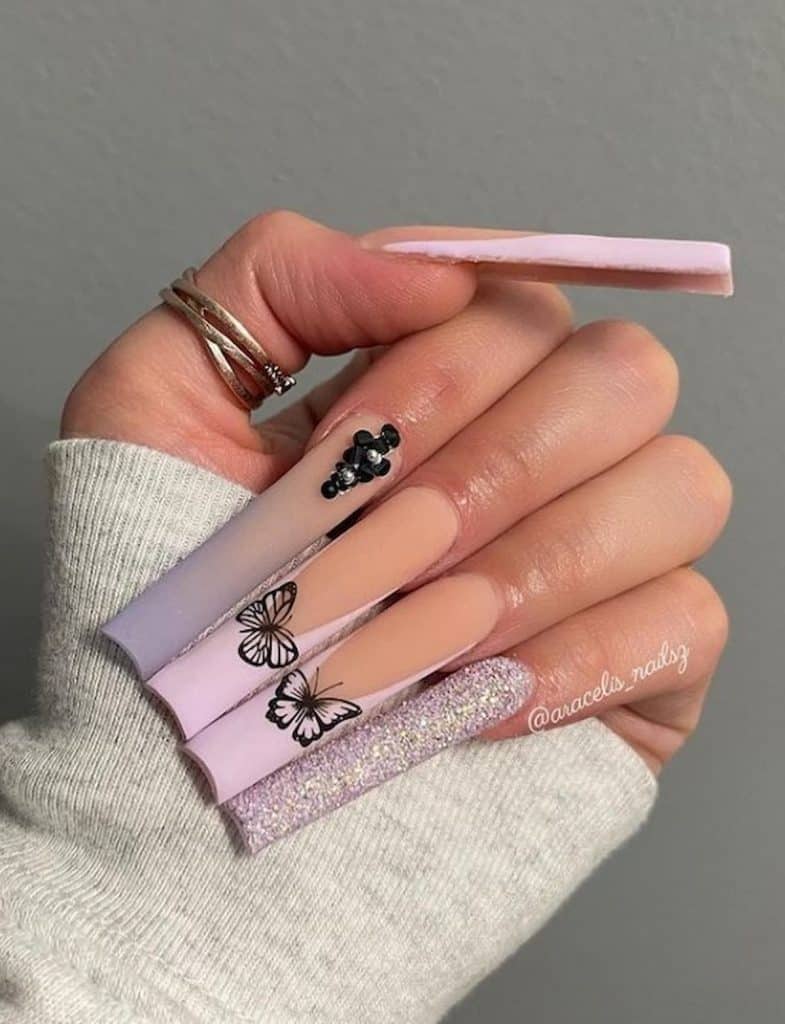A woman's hands with long pastel pink and gray nails having a glitter, ombre, french tips, jewels, and butterfly designs