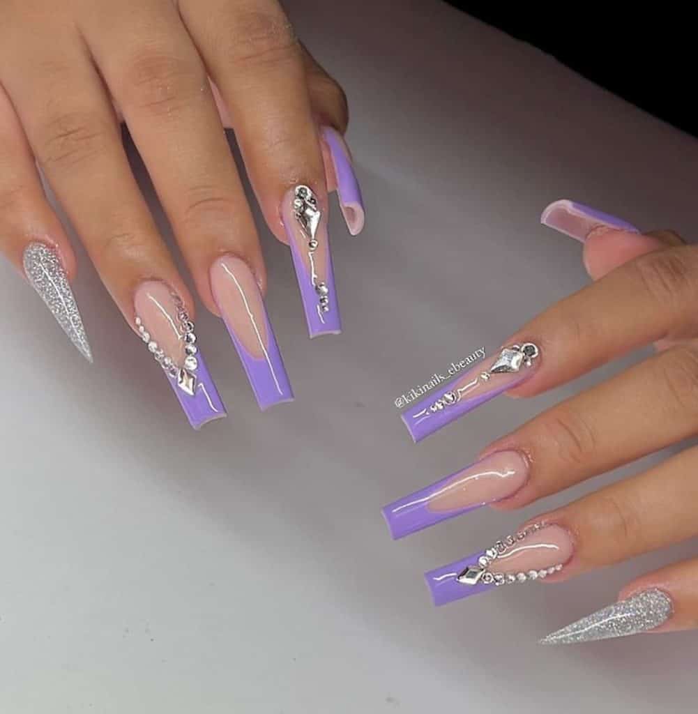 A woman's hands with lavender acrylic nails, glitters, and gem designs