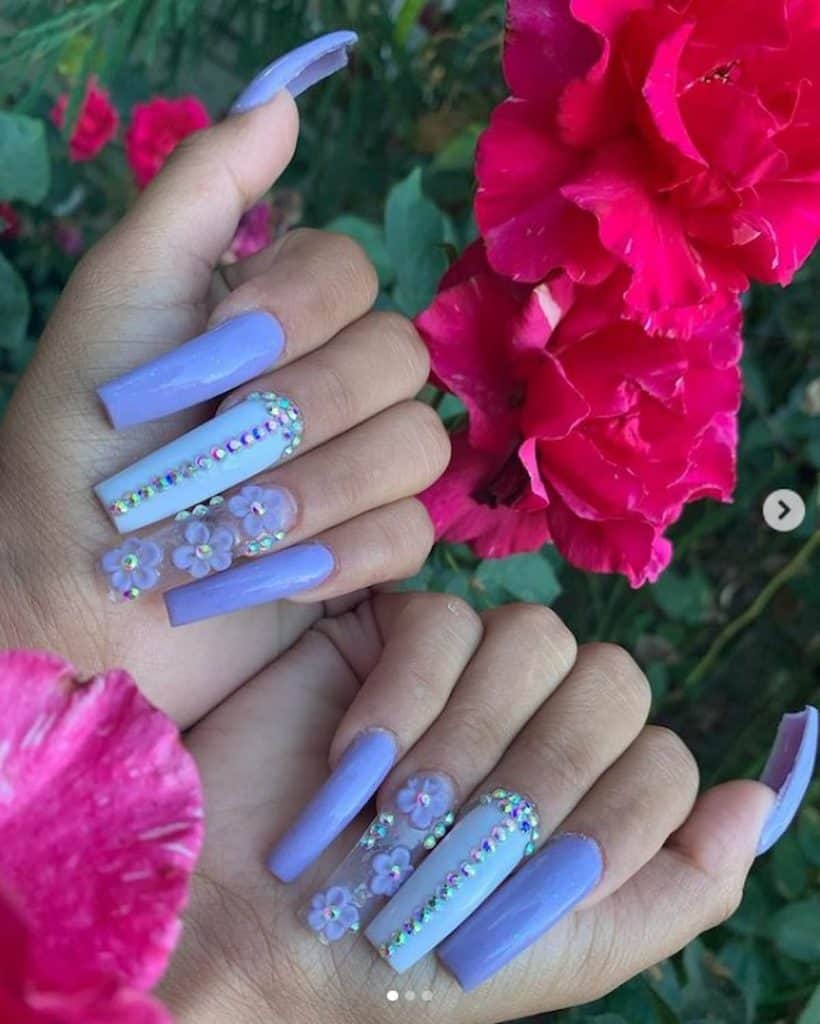 A woman's hands with blue lavender nails, rhinestones, and flower charm designs
