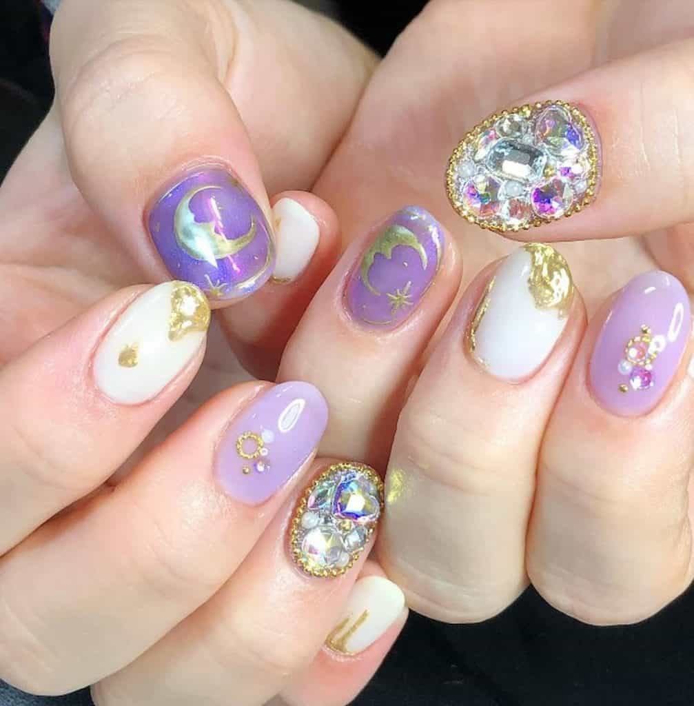 A woman's hands with a lavender and white colored nail polish. It has gold moons and sparkly crystal designs