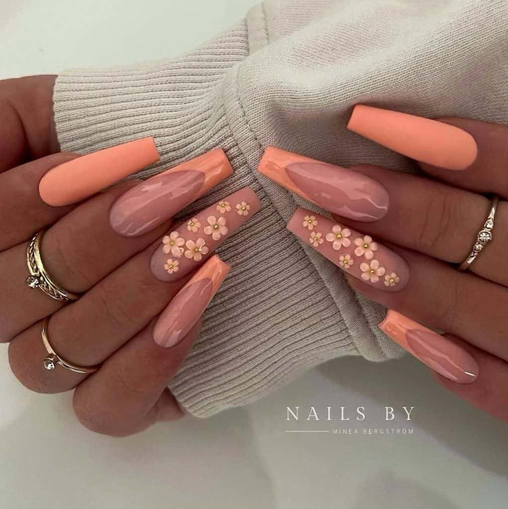 A woman's hands with matte and glossy peach and pink nail polish that has 3D peach-colored florals and French tips 