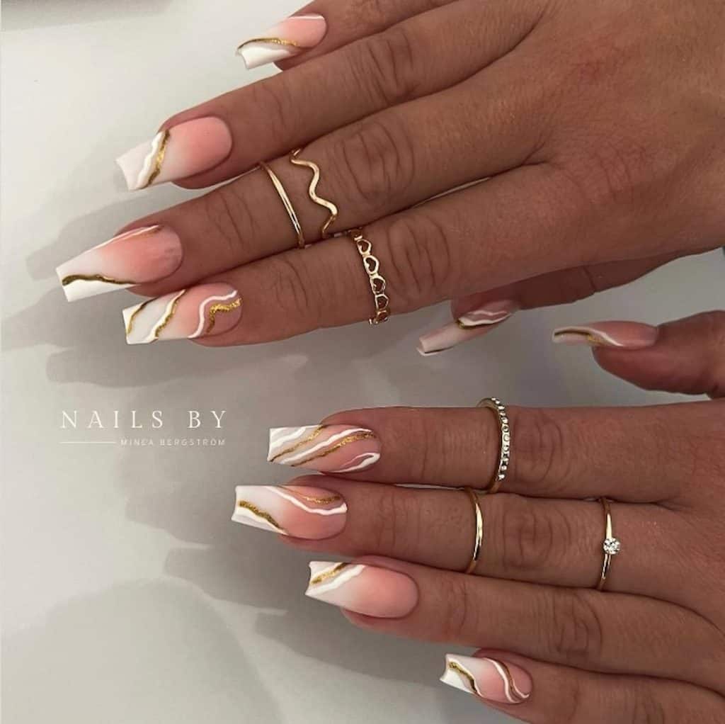 A woman's hands with beautiful with a combination of white, gold, and peach nail colors that has white and gold streaks