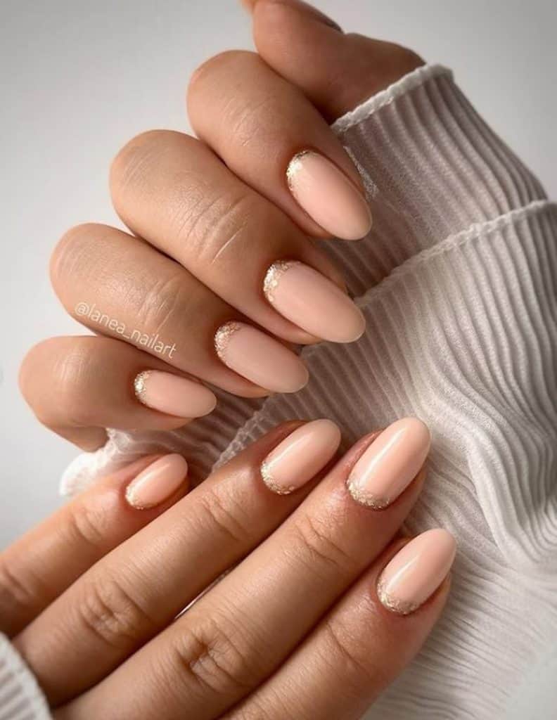 A closeup of a woman's hands with soft peach-colored nails that has rose gold glitters nail designs 