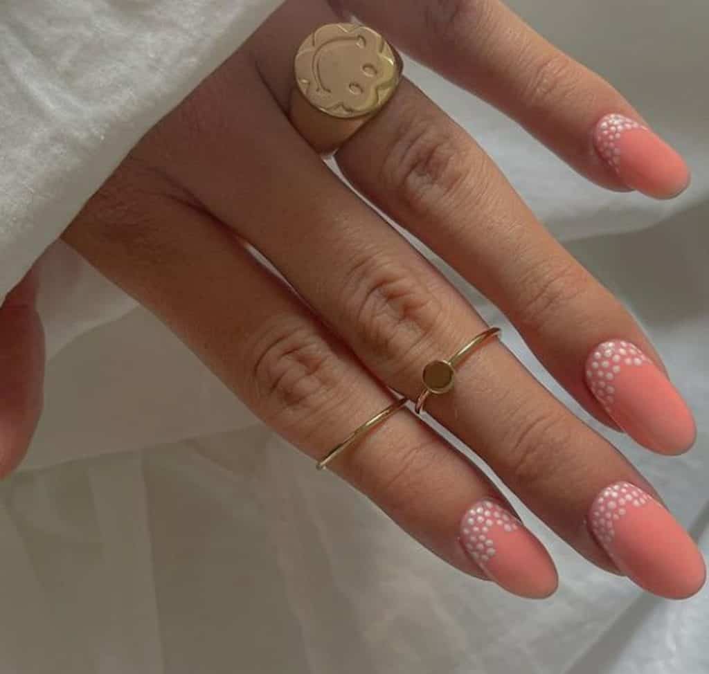 A closeup of a woman's hand with peach nail polish base that has white dots nail designs
