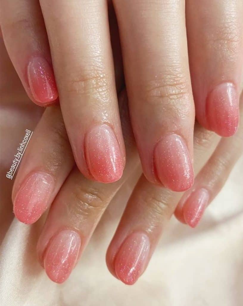 A closeup of a woman's hands with peachy pink ombre nails that has glitters for top coat