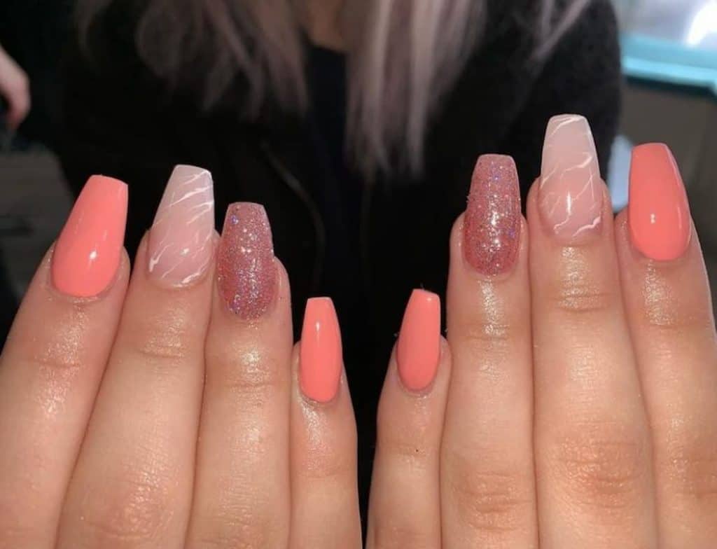 A closeup of a woman's hands with neon peach, marble texture and a glittery top coat 