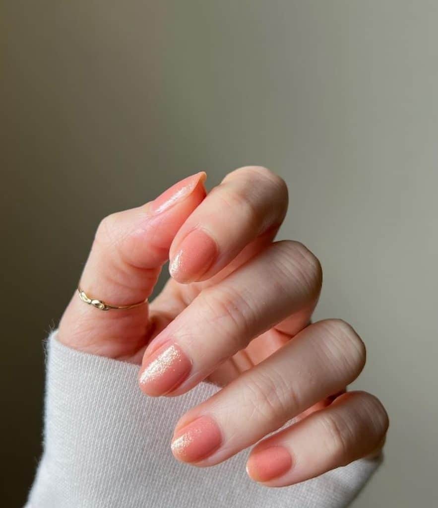 A closeup of a woman's hand with peach nail polish base that has a glittery top coat