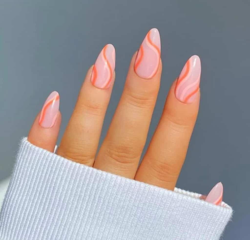 A closeup of a woman's hand with pink press-on nails with squiggly accents in two shades of peach