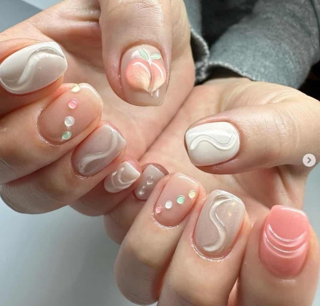 A closeup of a woman's hands with a combination of pink, peach, and taupe nails that has D water droplets, fun patterns, and a giant peach fruit nail designs