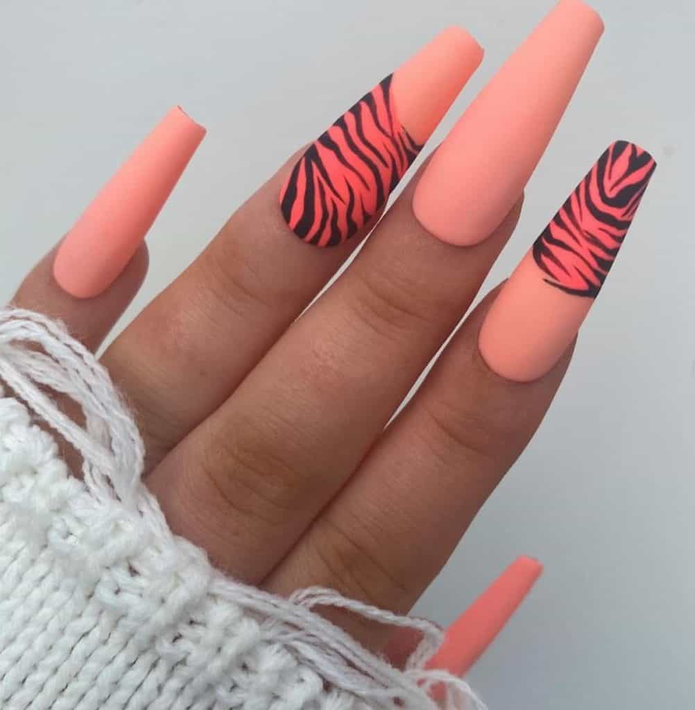 A closeup of a woman's hand with long coffin nails matte neon peach that has tiger prints 