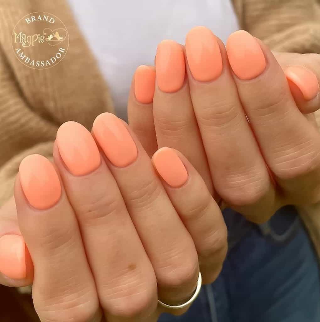 A closeup of a woman's hands with neon peach-colored round nails