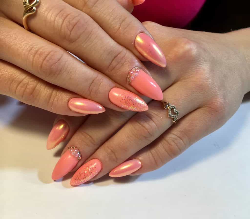 A woman's hands with beautiful chrome peach nails that has metallic glitters, rhinestones and pearls nail designs on select nails