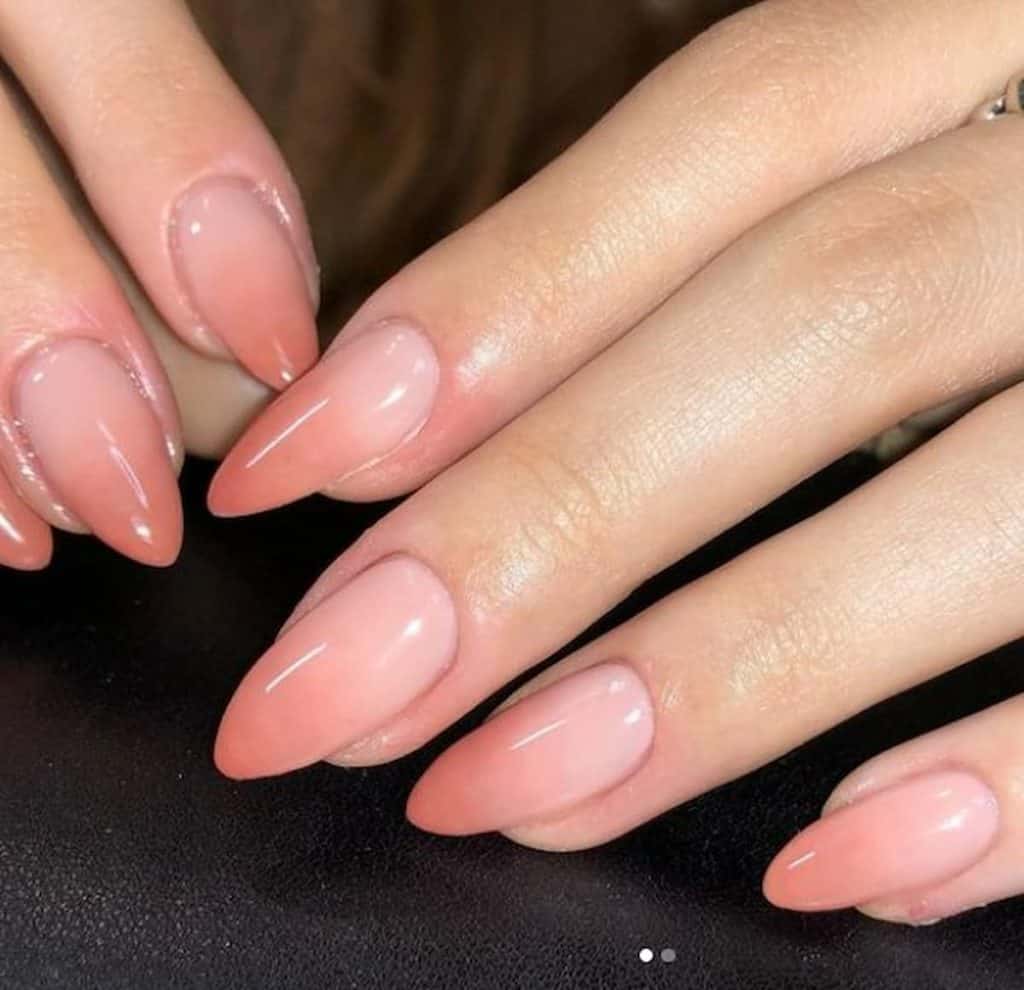 A closeup of a woman's hands with a mid-length stiletto nails in a peach ombre nail polish