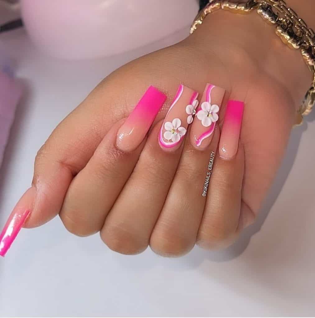 A closeup of a woman's hand with beautiful pink nail polish that has hot pink ombre tips, pink and white swirls, and 3D flower accents nail designs