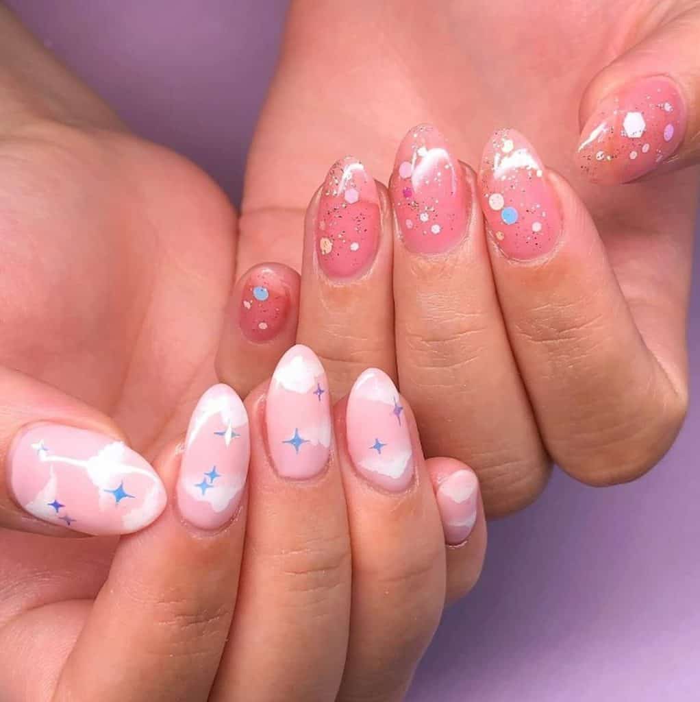 A closeup of a woman's hands that has light and blush pink nail polish that has stardust-like glitter, sequins, blue stars and clouds nail designs