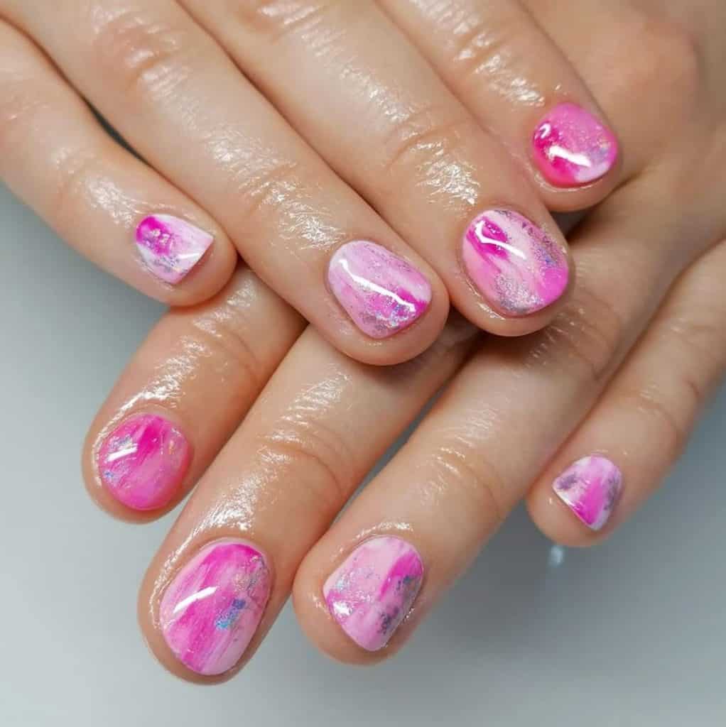 A closeup of a woman's hands with beautiful streaks of pink nail polish that has little glitter nail designs 