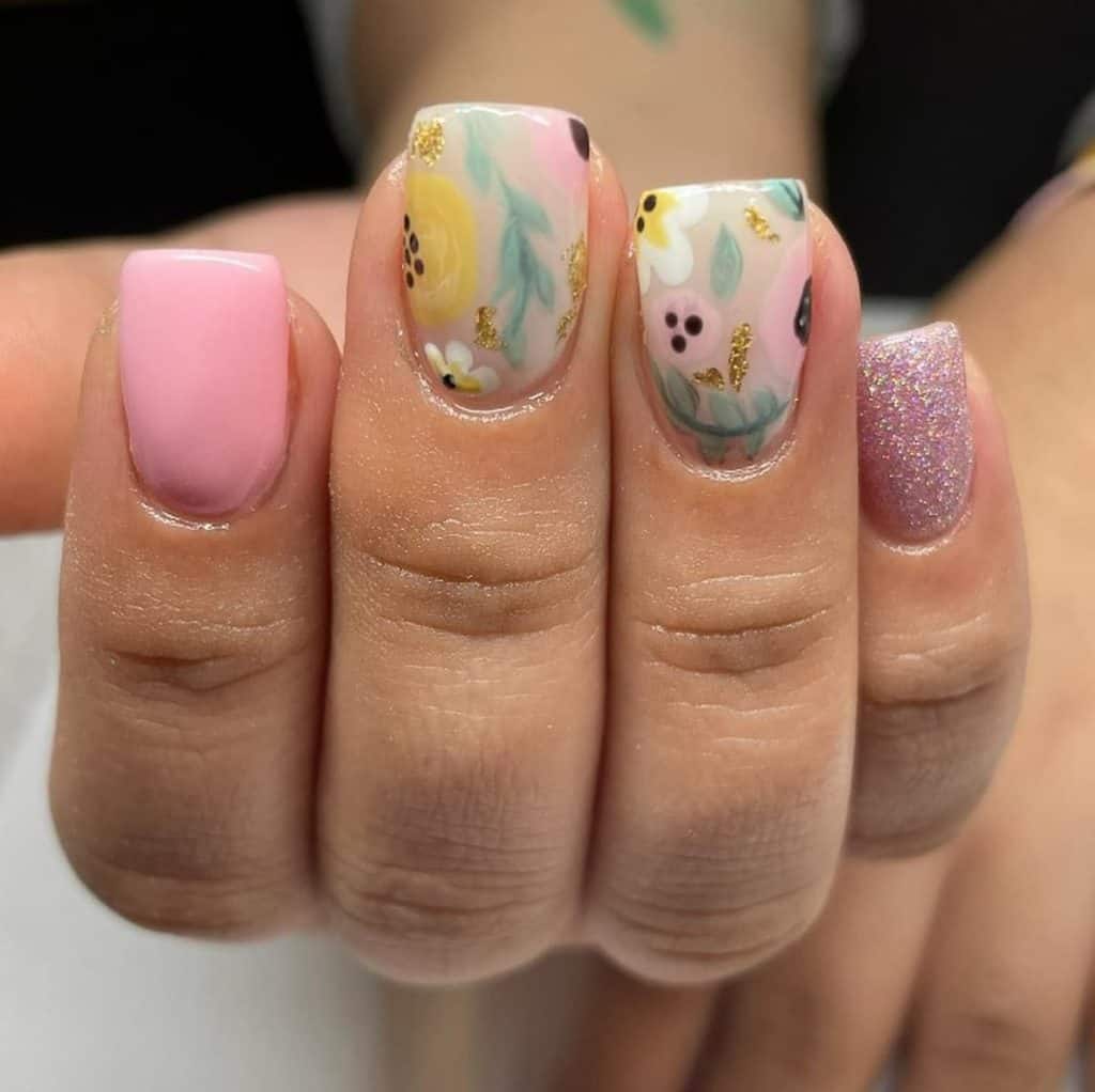 A closeup of a woman's hand with multicolored nail polish that has sparkly glitter, watercolor leaves and flowers nail designs 