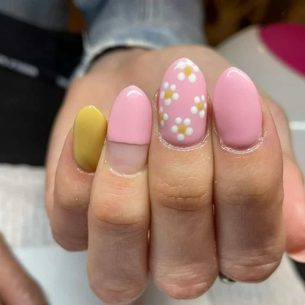 A closeup of a woman's hand with a combination of light pink and yellow nail polish that has lovely daisies nail design on the middle nail