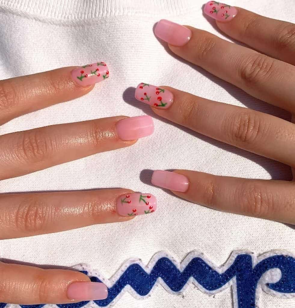 A woman's hands with beautiful pink nail polish that has cherries nail designs on select nails