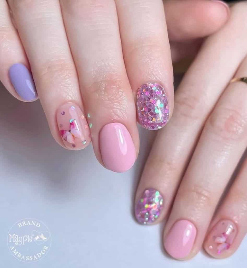 A closeup of a woman's hands with a combination of nude, pink and light blue nail polish that has sequins and stamped butterfly nail designs