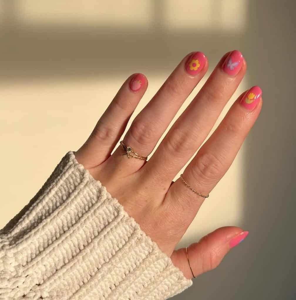 A woman's hand with beautiful pink polish that has stamp fruit, flower and butterfly nail designs