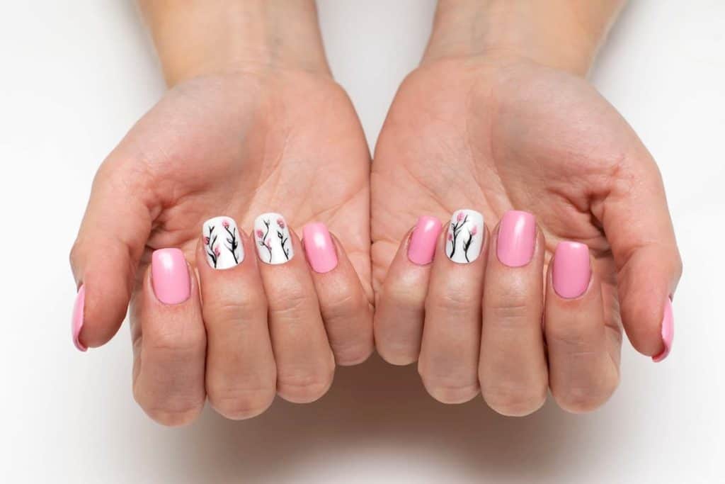 A woman's hands with a combination of white ang pink nail polish that has flowers as nail designs