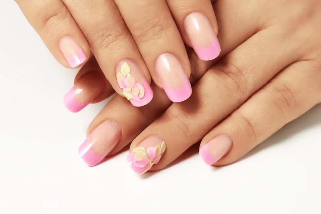 A closeup of a woman's hands with pink nail polish that has pink ombré-colored spring petals nail designs