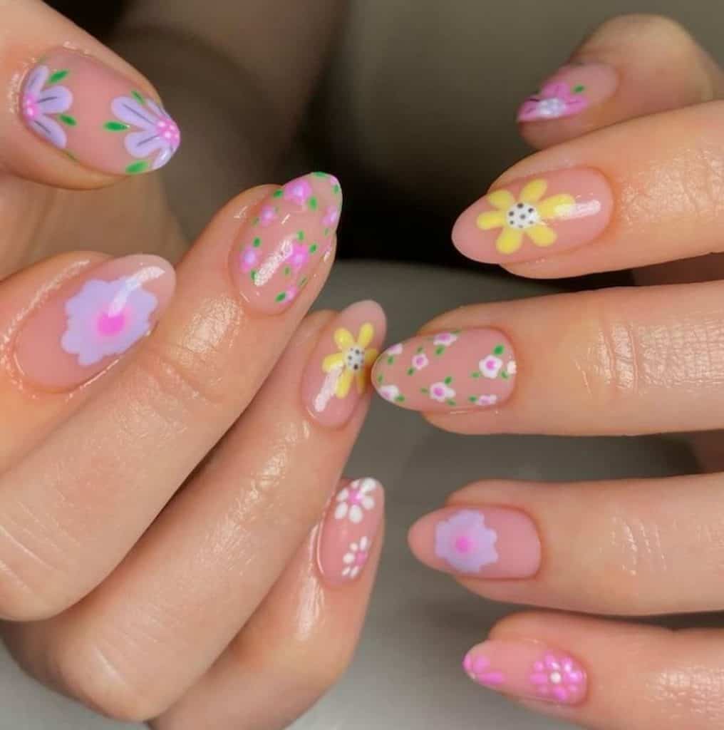 A closeup of a woman's hands with a beautiful nude pink nail polish that has different type of flowers nail designs