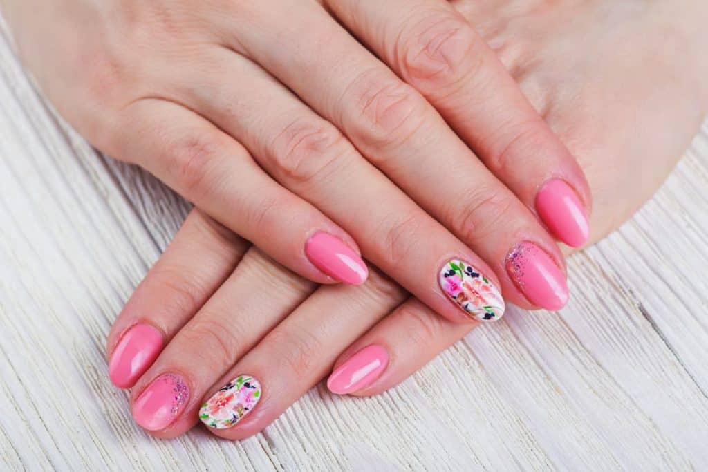 A closeup of a woman's hands with a combination of pink and white nails that has hand-painted flowers, leaves and glitter nail designs