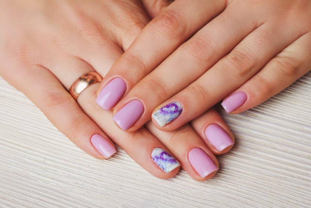 A woman's beautiful hands with classic pink and white nail polish that has purple marble texture on select nails 