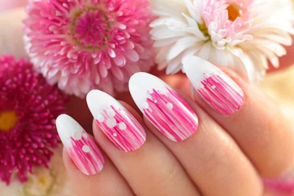 A closeup of a woman's hand with a beautiful pink nail polish and white tips, holding a flower