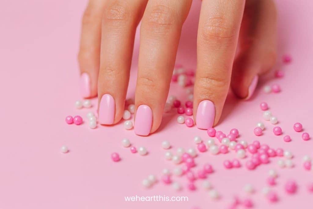 A closeup of a woman's hand with pink nail polish isolated on a pink background
