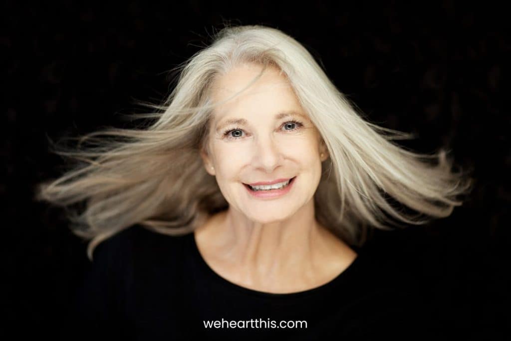 Stunning beautiful and self confident best aged woman with grey hair smiling into camera, portrait with black background 