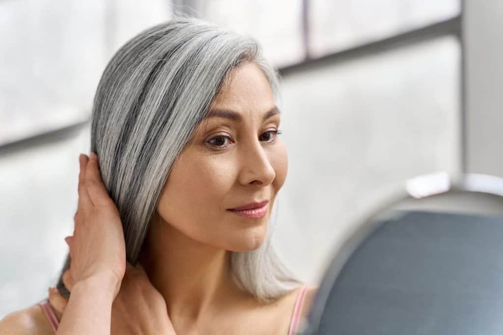 A woman is brushing her gray hair in front of a mirror.