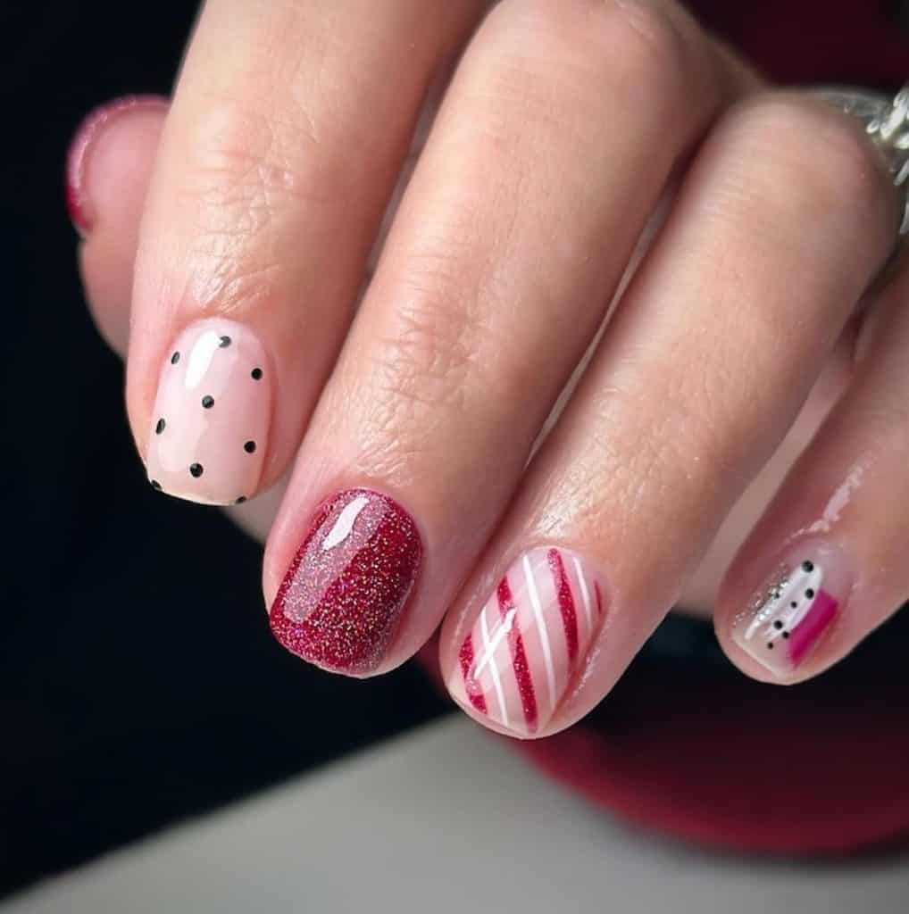 A closeup of a woman's hand with a combination of nude, white and red nail polish base that has polka dots, stripes, abstract, and glitter nail designs