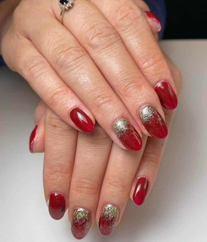 A woman's hands with red nail polish that has white gold glitter powder nail designs
