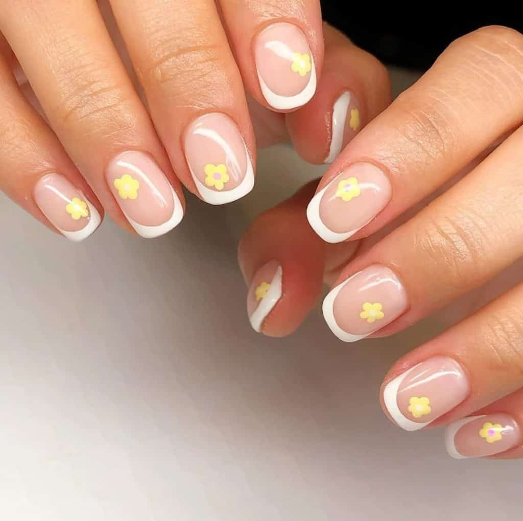A woman's hands with nude nail polish and white nail tips that has yellow flowers nail designs