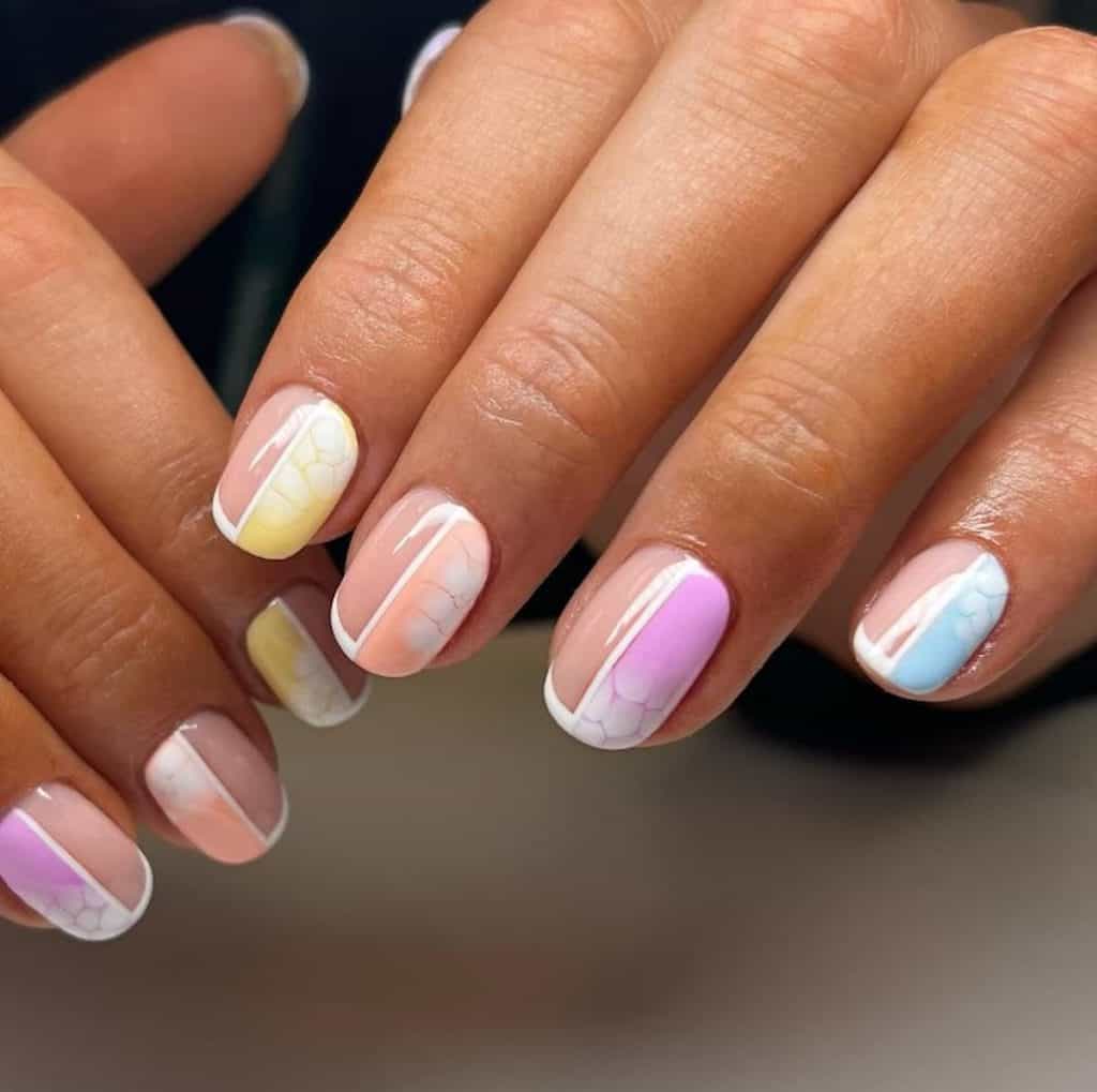 A closeup of a woman's hands with multicolored nail polish that has ombré pastels and solid white lines and croc print nail designs