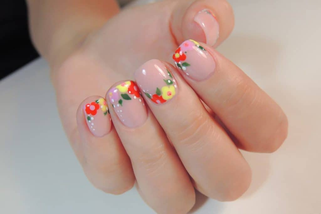 A woman's hands with nude nail polish that has floral and leaves nail designs