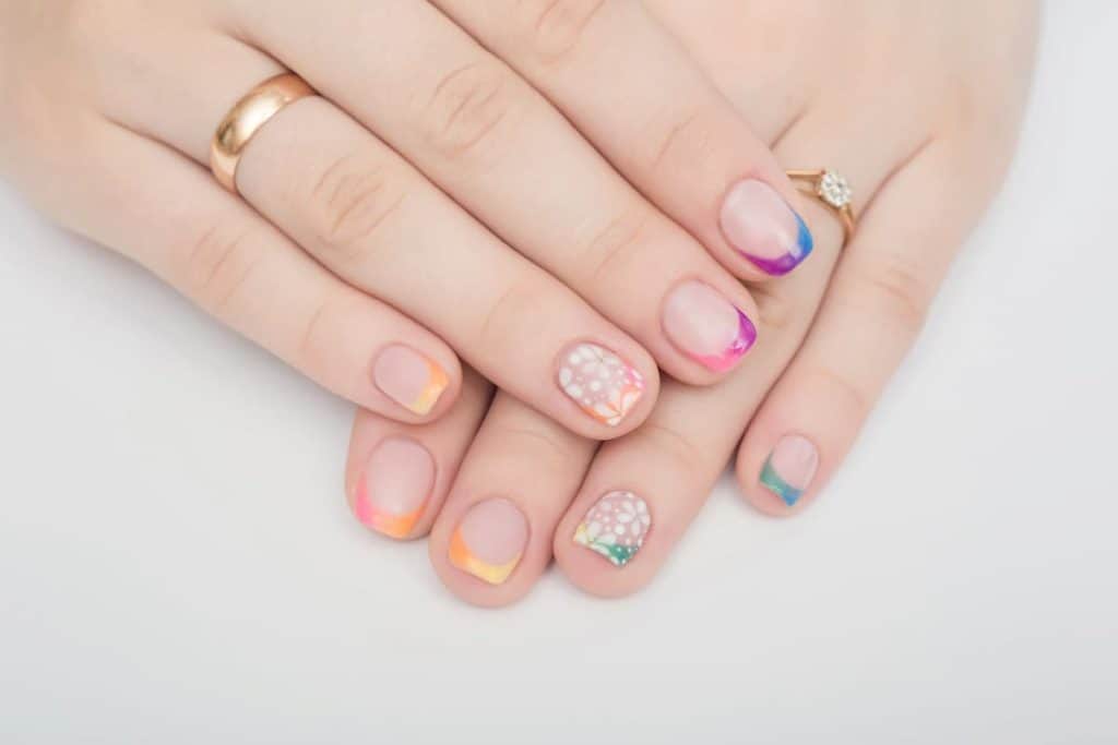 A closeup of a woman's hands with nude nail polish that has Gradient tips, rainbow hues, and pinwheel florals nail designs