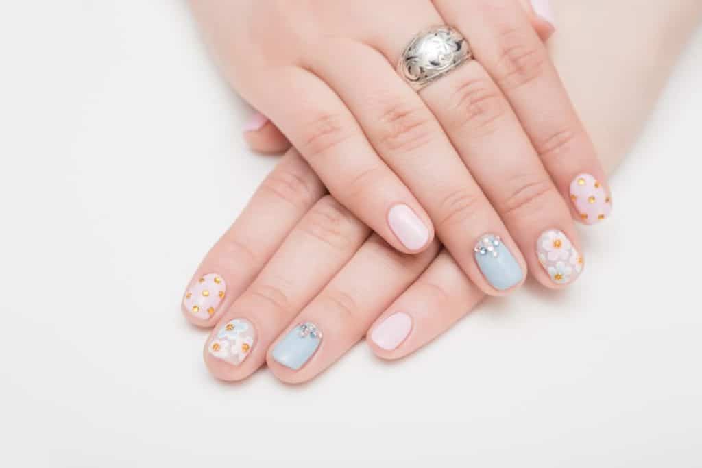 A woman's beautiful hands with blue and white nail polish that has flowers and gems nail designs on select nails