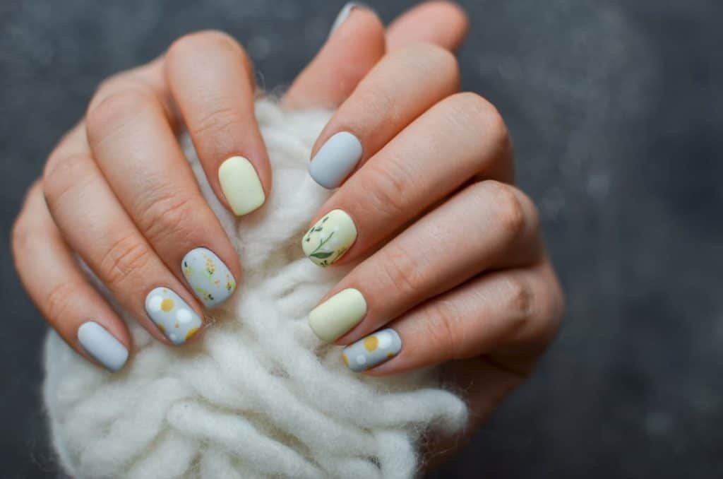 A closeup of a woman's hands with light yellow and blue nail polish that has floral nail designs on select nails