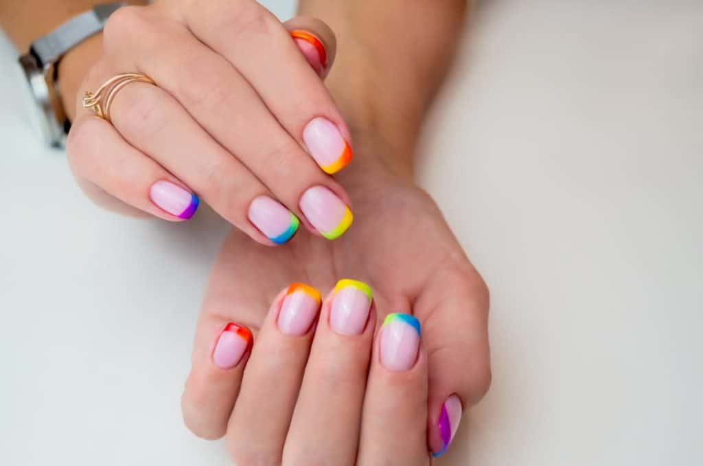 A woman's hands with nude nail polish that has multicolored nail tips 