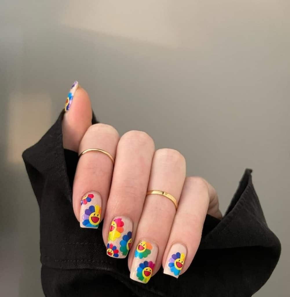 A closeup of a woman's hand wearing a ring with white nail polish that has rainbow sunflower, smiling nail designs
