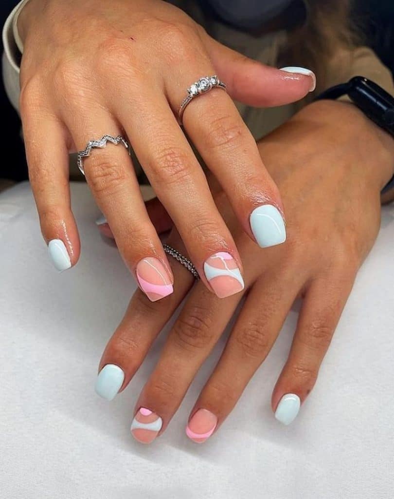 A woman's beautiful hands with a combination of nude, pink, and blue nail polish that has a swirl nail designs