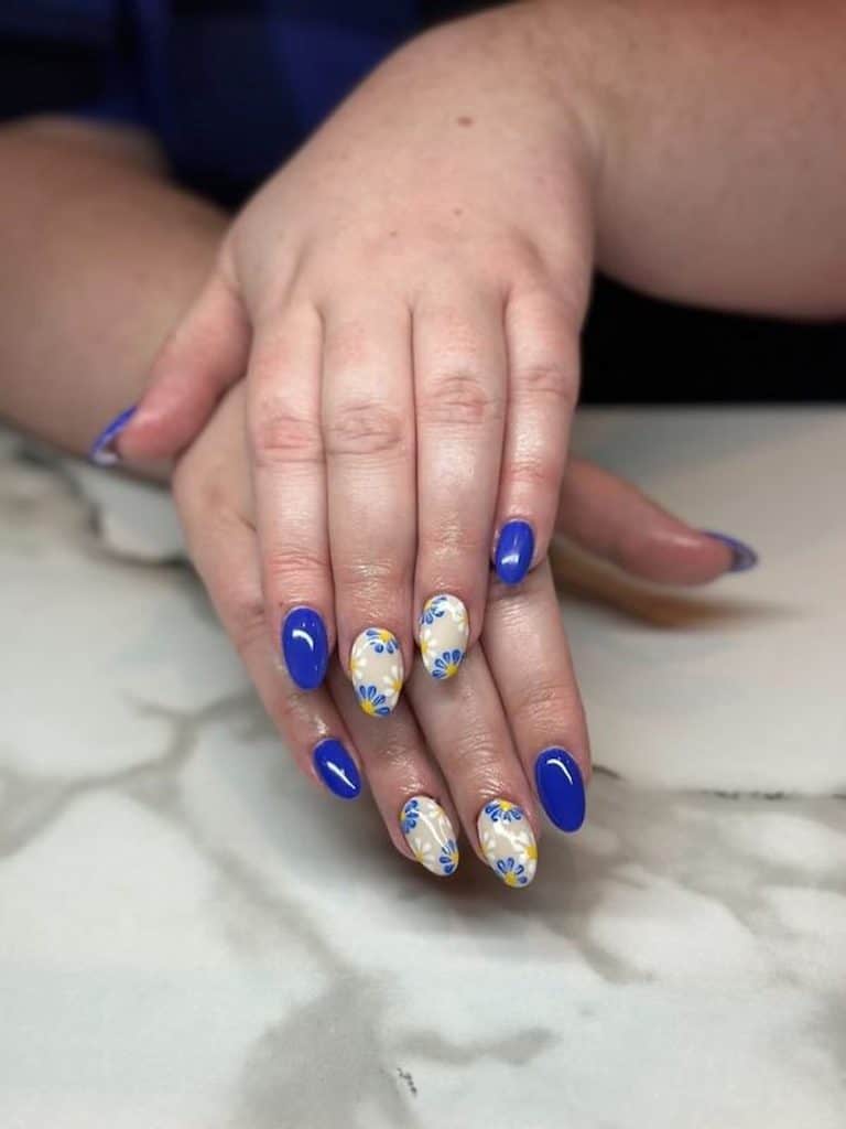 A woman's hands with a combination of white and blue nail polish that has accents of yellow and white blooms nail designs