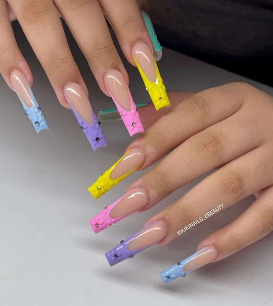 A woman's hands with long coffin nails and nude nail polish base that has soft-colored tips and studded flowers nail designs