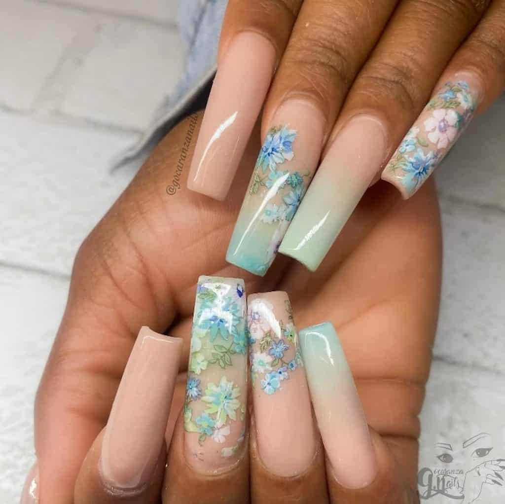 A closeup of a woman's hands with long nails that combines nude and mint green together that has white and blue flower stamps nail designs